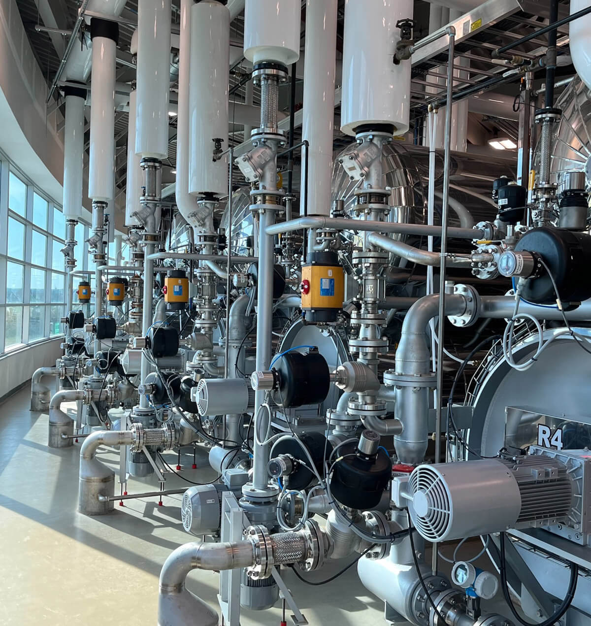 A line of canning retort machines beside a wall of windows.